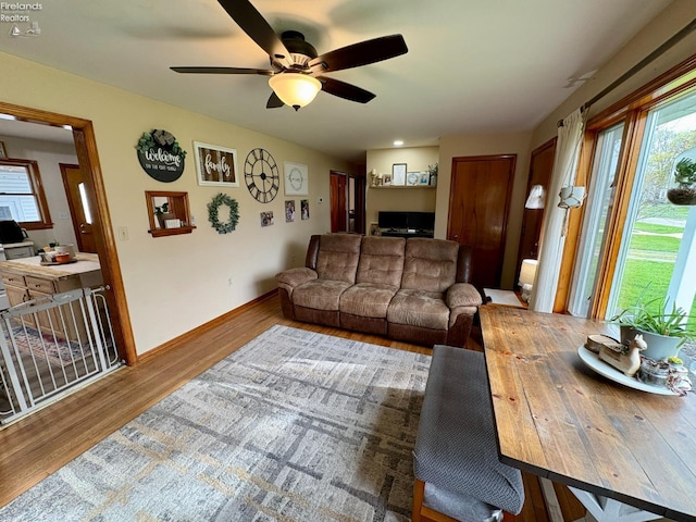 living area with baseboards, wood finished floors, and ceiling fan