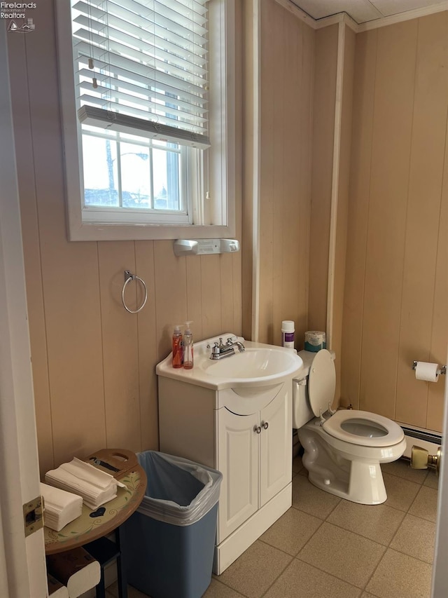 half bath with a baseboard radiator, toilet, vanity, and a decorative wall