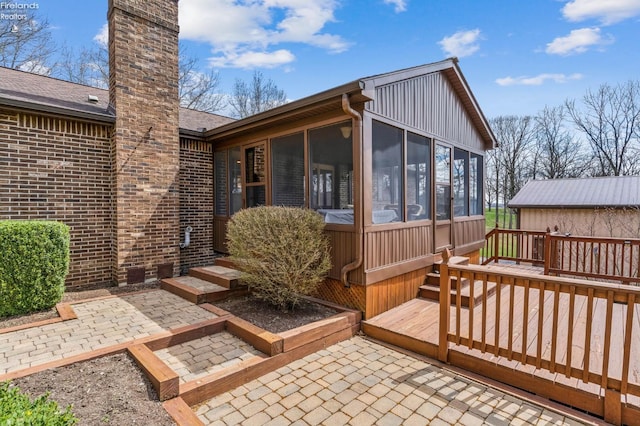 back of property featuring a wooden deck, a chimney, a sunroom, and brick siding