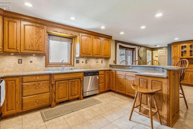 kitchen with a peninsula, stainless steel dishwasher, brown cabinets, and a kitchen breakfast bar
