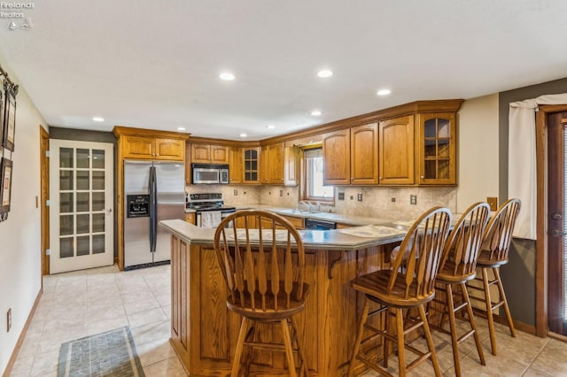 kitchen featuring stainless steel appliances, baseboards, recessed lighting, glass insert cabinets, and brown cabinetry