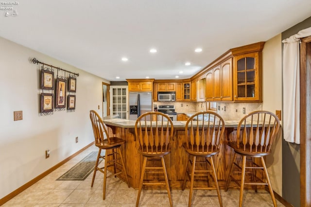 interior space with brown cabinetry, glass insert cabinets, a peninsula, appliances with stainless steel finishes, and recessed lighting