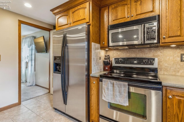 kitchen featuring brown cabinets, decorative backsplash, light tile patterned floors, light countertops, and appliances with stainless steel finishes