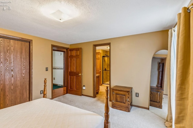 bedroom featuring a textured ceiling, a closet, connected bathroom, arched walkways, and light carpet