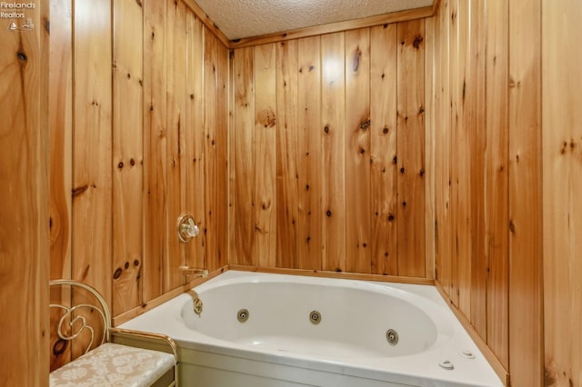 bathroom featuring wooden walls, a textured ceiling, and a tub with jets