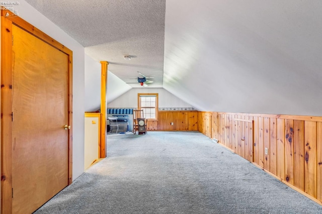 bonus room with a textured ceiling, vaulted ceiling, wood walls, ceiling fan, and carpet floors