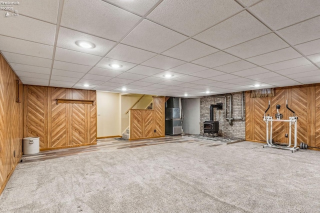 finished below grade area featuring a wood stove, carpet flooring, wood walls, and heating unit