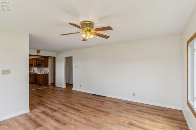 unfurnished living room featuring visible vents, a sink, light wood-style floors, baseboards, and ceiling fan
