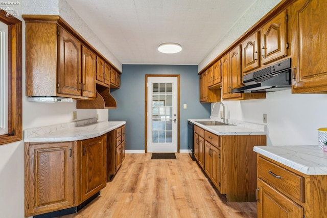 kitchen with a sink, brown cabinetry, light countertops, under cabinet range hood, and black dishwasher