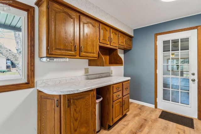 kitchen with brown cabinetry, a wealth of natural light, light wood finished floors, and baseboards