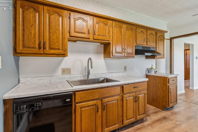 kitchen with a sink, brown cabinets, light countertops, under cabinet range hood, and black dishwasher