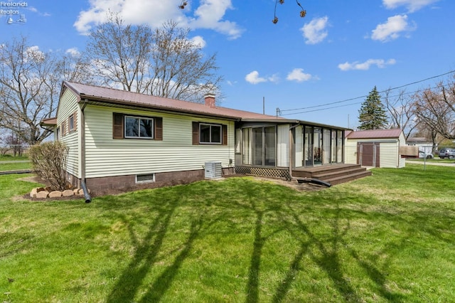 back of house featuring a chimney, an outdoor structure, a yard, a sunroom, and a storage unit