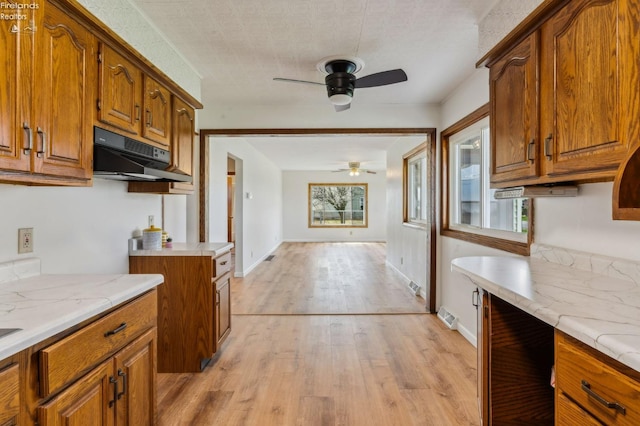 kitchen featuring brown cabinetry, ceiling fan, under cabinet range hood, and light countertops