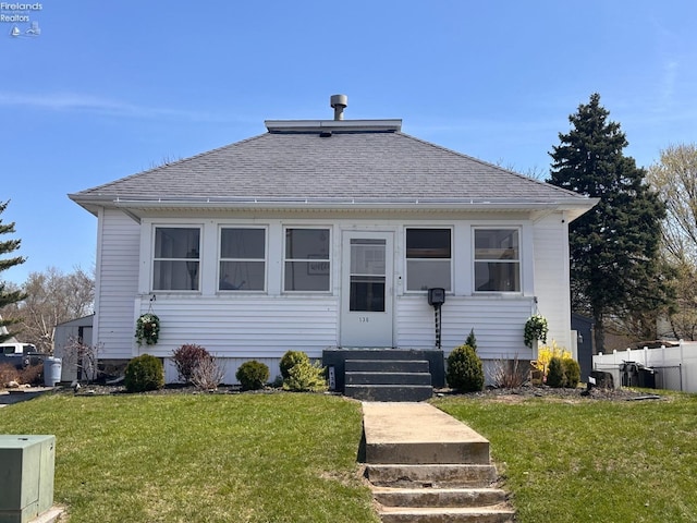 bungalow-style home featuring fence, a front lawn, and roof with shingles