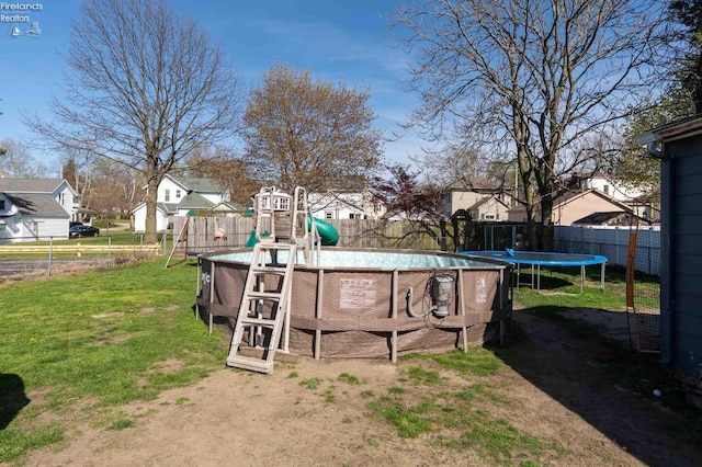 view of swimming pool with a residential view, a trampoline, and a fenced backyard