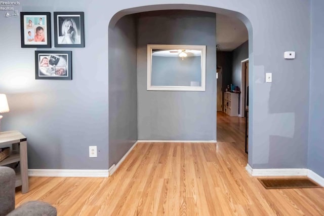 hallway featuring arched walkways, wood finished floors, and baseboards