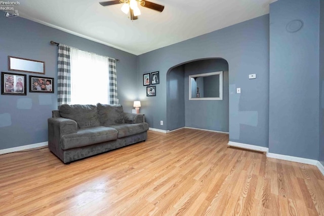 living area with arched walkways, wood finished floors, baseboards, and ceiling fan