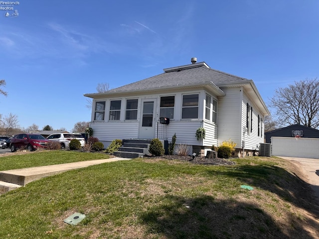 bungalow-style home with a detached garage, an outbuilding, a front yard, and central AC