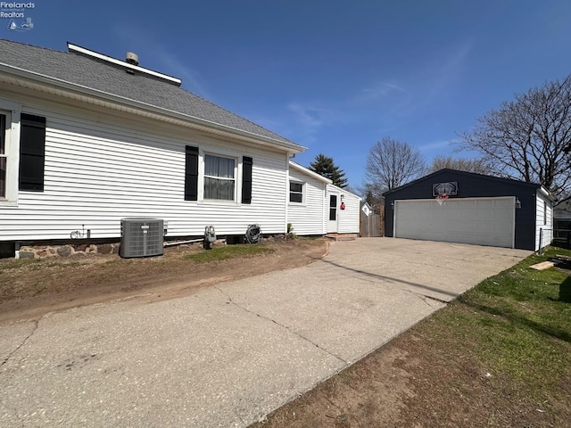 view of side of property featuring an outbuilding, cooling unit, a shingled roof, and a garage