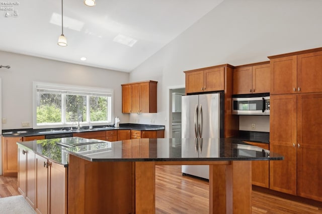 kitchen featuring appliances with stainless steel finishes, a sink, brown cabinetry, light wood-type flooring, and a kitchen island