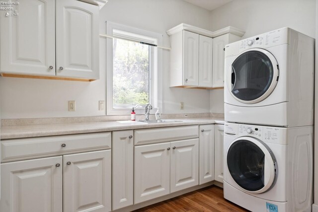 laundry room featuring cabinet space, stacked washer and dryer, a sink, and wood finished floors
