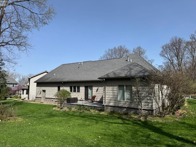 rear view of property with a lawn, roof with shingles, central AC unit, and a patio area