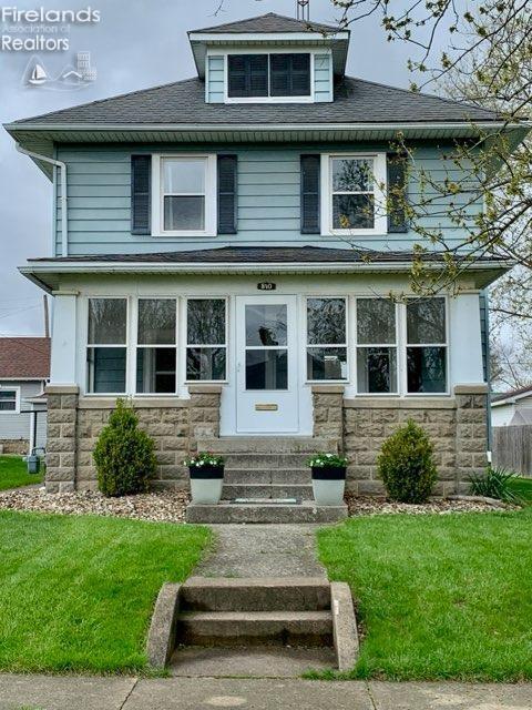traditional style home featuring entry steps, roof with shingles, stone siding, and a front lawn
