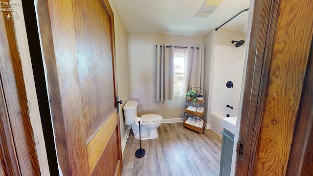 full bath featuring toilet, wood finished floors, shower / tub combination, and baseboards