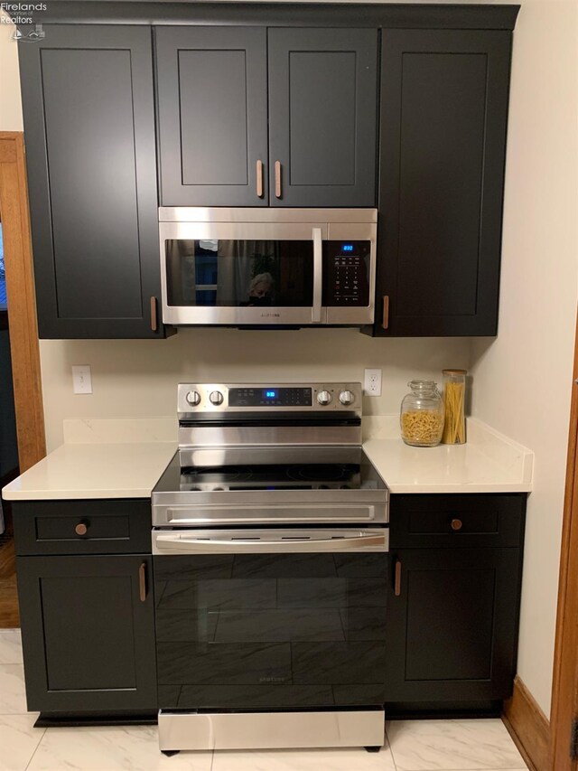 kitchen with marble finish floor, light countertops, appliances with stainless steel finishes, and baseboards