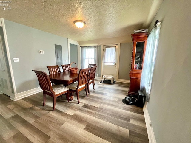 dining room with baseboards, a textured ceiling, and light wood-style flooring