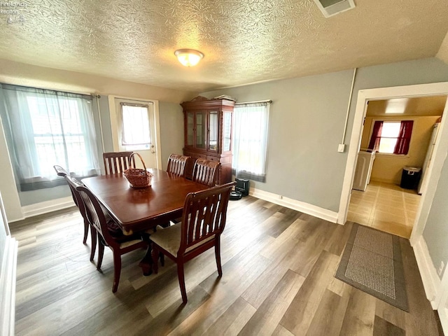 dining area with visible vents, a textured ceiling, baseboards, and wood finished floors