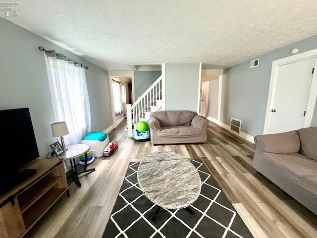 living room featuring baseboards, a textured ceiling, stairs, and wood finished floors