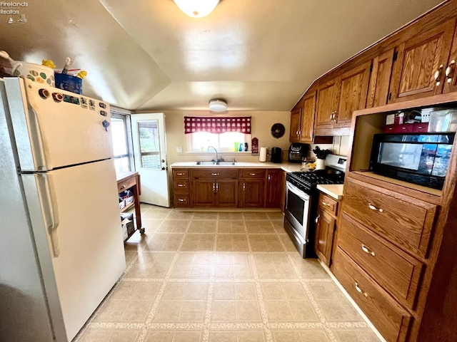 kitchen featuring brown cabinets, stainless steel gas stove, a sink, light countertops, and freestanding refrigerator