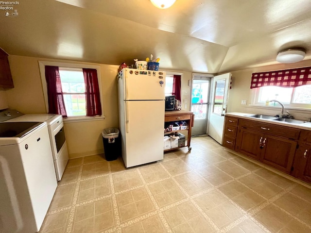 kitchen with a sink, light countertops, freestanding refrigerator, lofted ceiling, and washer and dryer