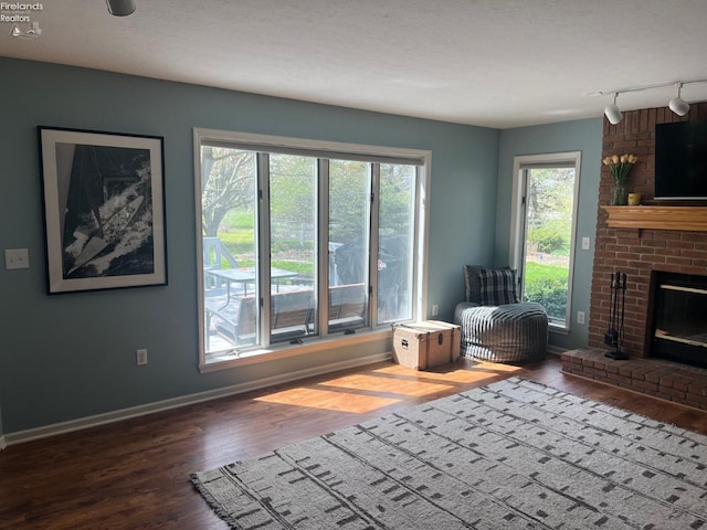 living area with baseboards, track lighting, wood finished floors, and a brick fireplace