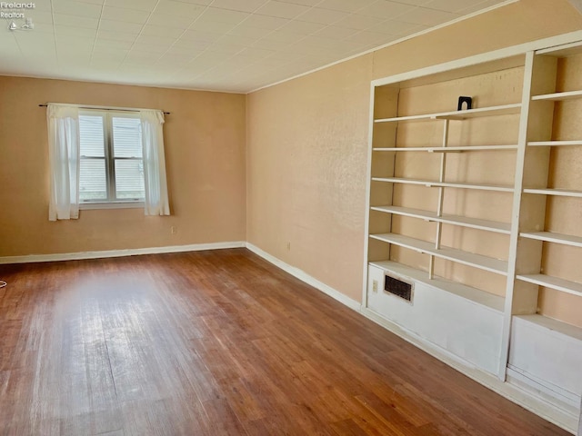 empty room with baseboards, wood finished floors, and built in features
