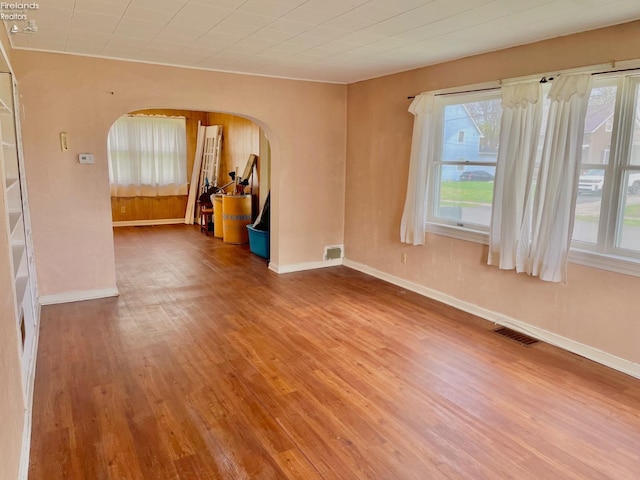 spare room featuring arched walkways, wood finished floors, visible vents, and baseboards
