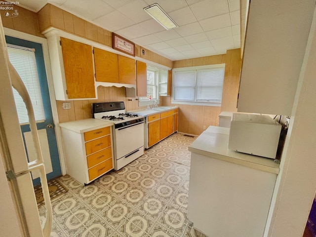 kitchen with brown cabinetry, wood walls, white gas range, and light countertops