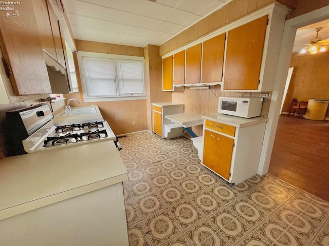 kitchen featuring a ceiling fan, a sink, white appliances, light countertops, and wood walls