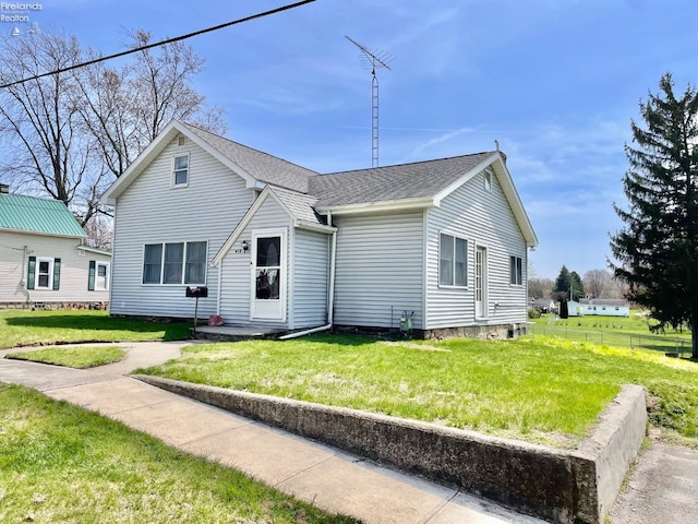 rear view of house with a lawn, fence, and roof with shingles