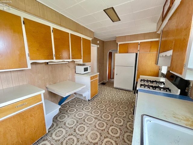 kitchen with brown cabinetry, wood walls, white appliances, and light countertops