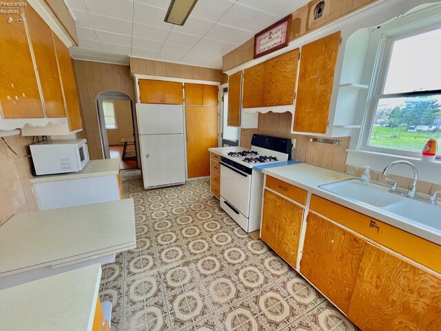 kitchen featuring brown cabinetry, arched walkways, white appliances, and a sink