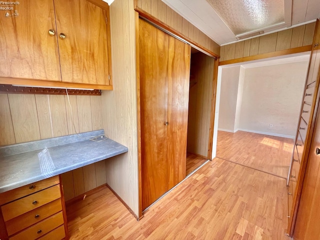 unfurnished office featuring light wood-type flooring, wood walls, and built in desk