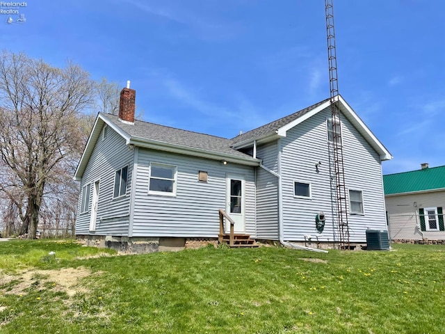 rear view of house with a chimney, entry steps, a yard, central air condition unit, and roof with shingles