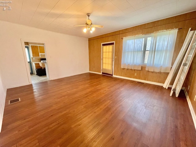 empty room with wood walls, wood finished floors, visible vents, and ceiling fan