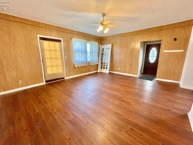 interior space with baseboards, wooden walls, wood finished floors, and ceiling fan