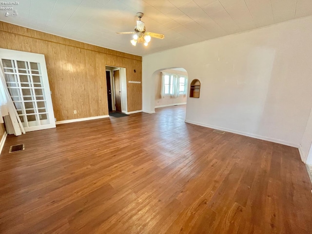 empty room featuring ceiling fan, arched walkways, wood finished floors, and baseboards