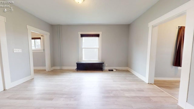 spare room featuring baseboards, radiator heating unit, and light wood finished floors