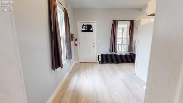 corridor with radiator, a wealth of natural light, light wood-style floors, and baseboards