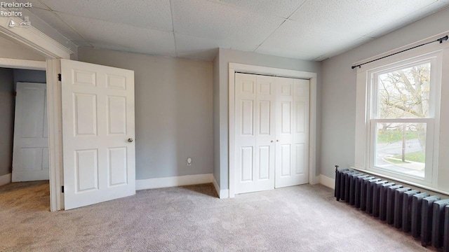 unfurnished bedroom with light colored carpet, radiator heating unit, multiple windows, and a closet